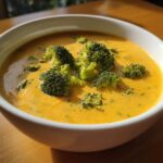 A close-up of thick, creamy Copycat Broccoli Cheddar Soup topped with bright green broccoli florets in a white bowl.