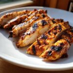 Close-up of perfectly sliced Copycat Chipotle Chicken breasts with visible char marks on a white plate.