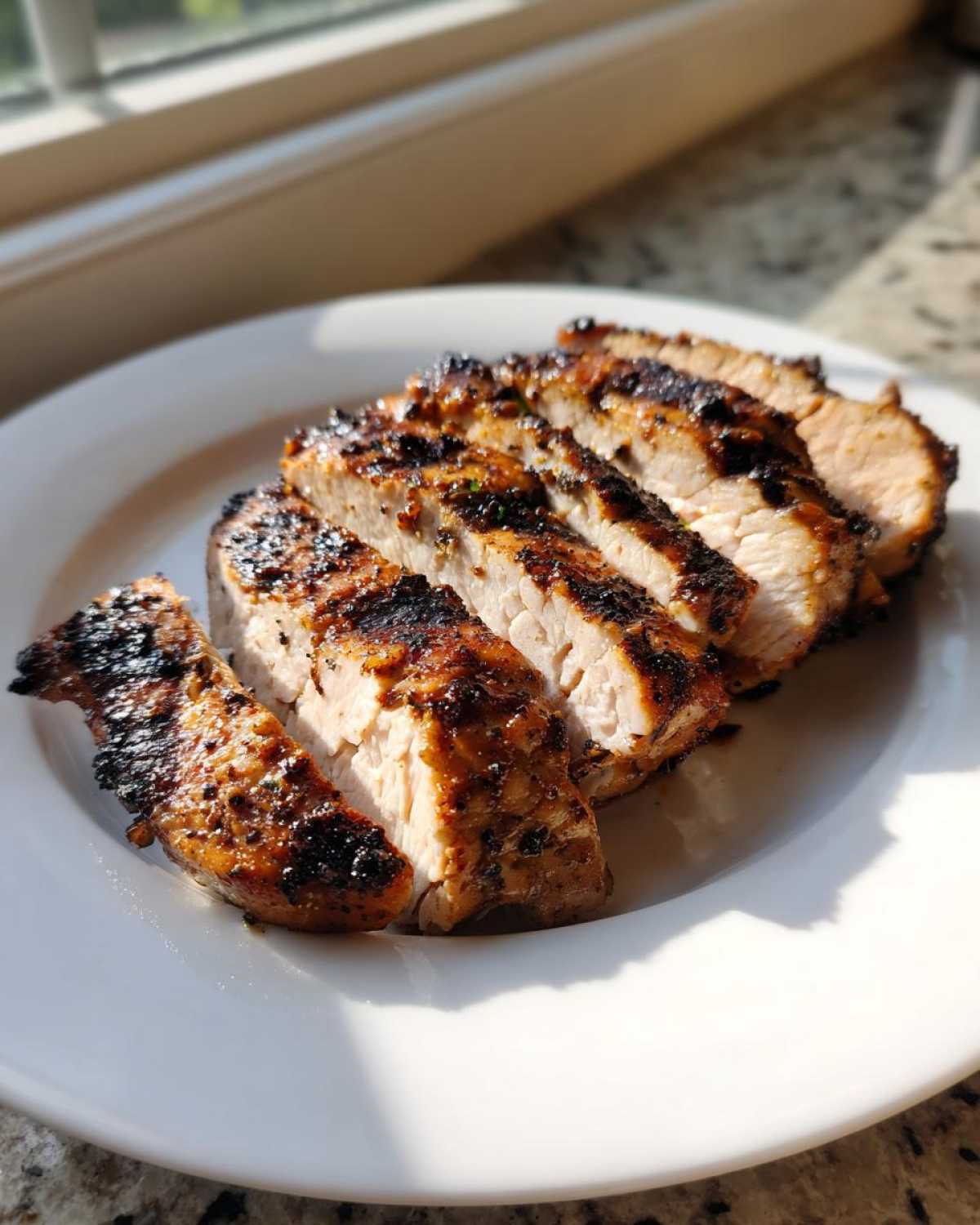 Slices of juicy Copycat Chipotle Chicken, showing a nicely charred exterior and white interior, served on a white plate.