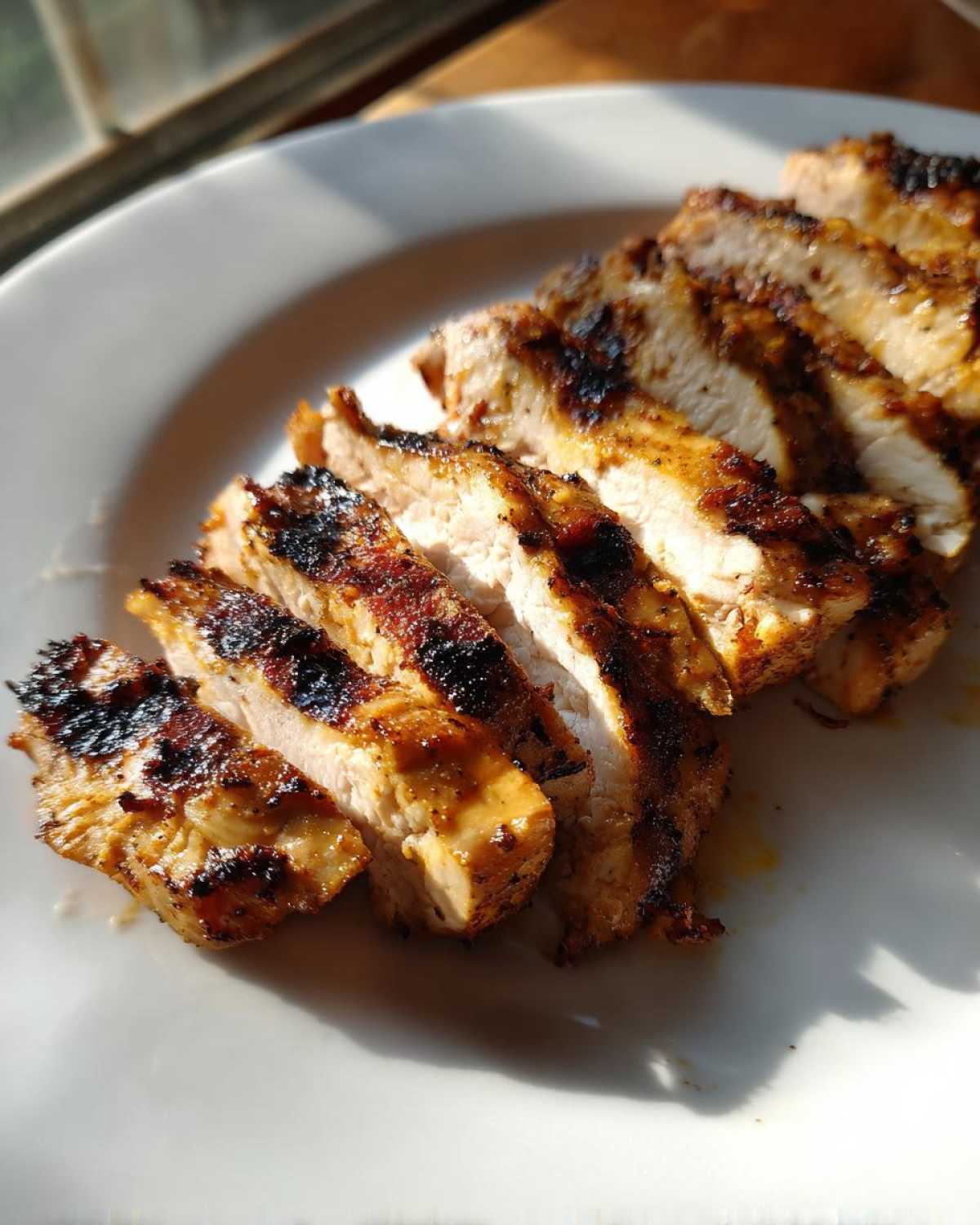 Slices of perfectly cooked Copycat Chipotle Chicken showing juicy white meat and dark char marks on a white plate.
