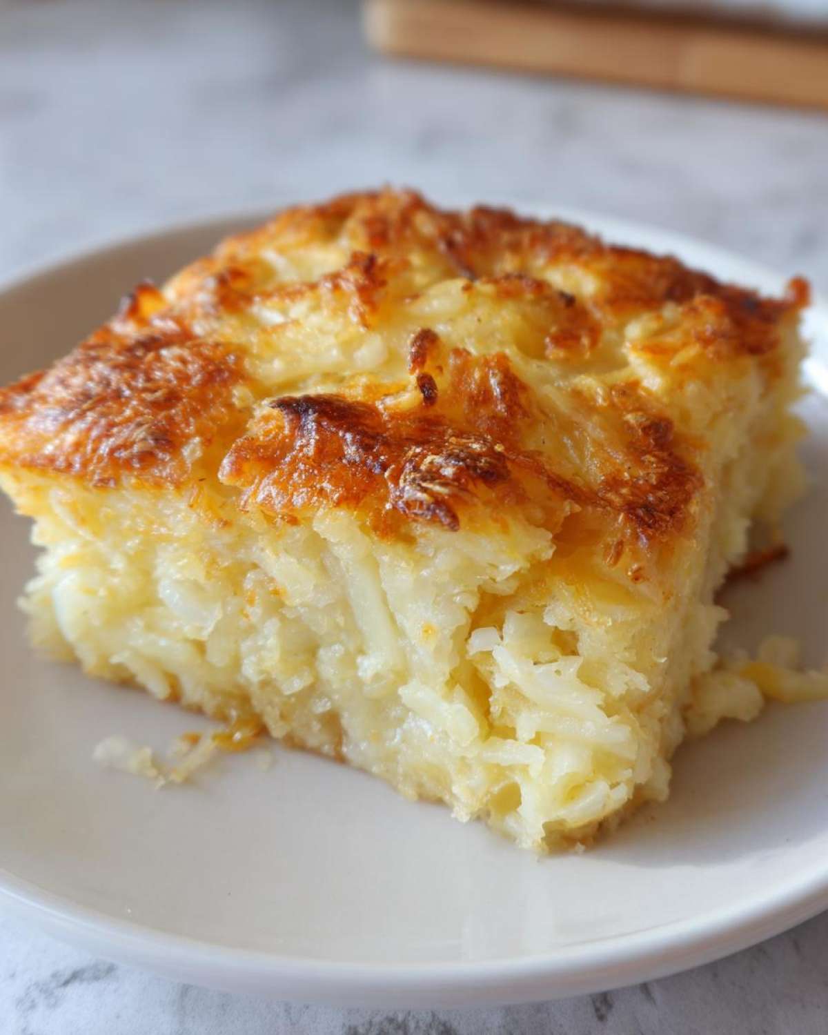 A square serving of creamy Copycat Cracker Barrel Hashbrown Casserole with a golden-brown, cheesy top.