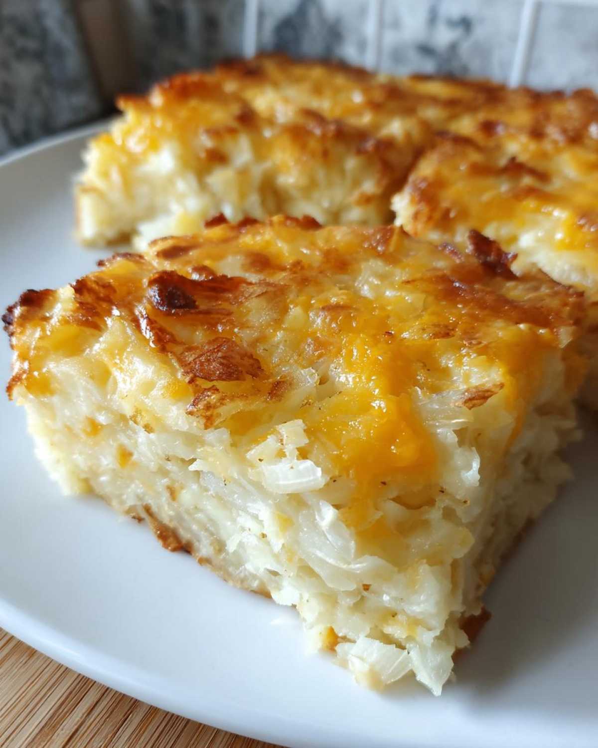 Close-up of a square slice of Copycat Cracker Barrel Hashbrown Casserole with melted, browned cheese topping.