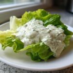 A dollop of creamy Copycat Olive Garden Salad Dressing generously topping a crisp piece of romaine lettuce on a white plate.
