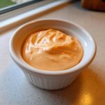 Close-up of thick, creamy, orange-hued Copycat Raising Cane’s Sauce served in a small white ramekin.