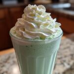 Close-up of a green Copycat Shamrock Shake with a tall swirl of white mint whipped cream on top.