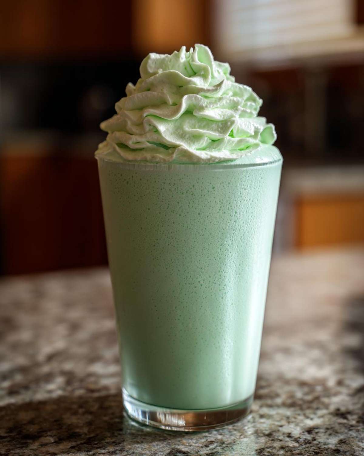 A tall glass filled with a pale green Copycat Shamrock Shake topped generously with mint whipped cream.
