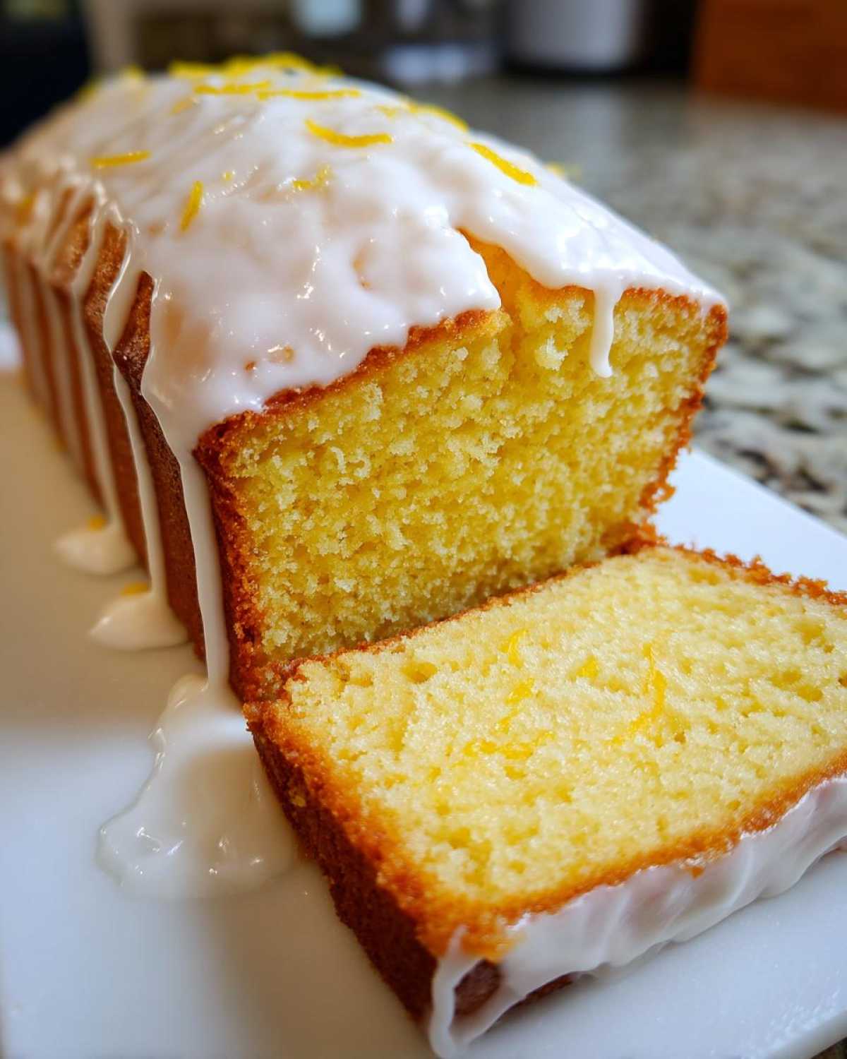A close-up of a moist Copycat Starbucks Iced Lemon Loaf, sliced, showing the thick white glaze dripping down the sides and lemon zest on top.