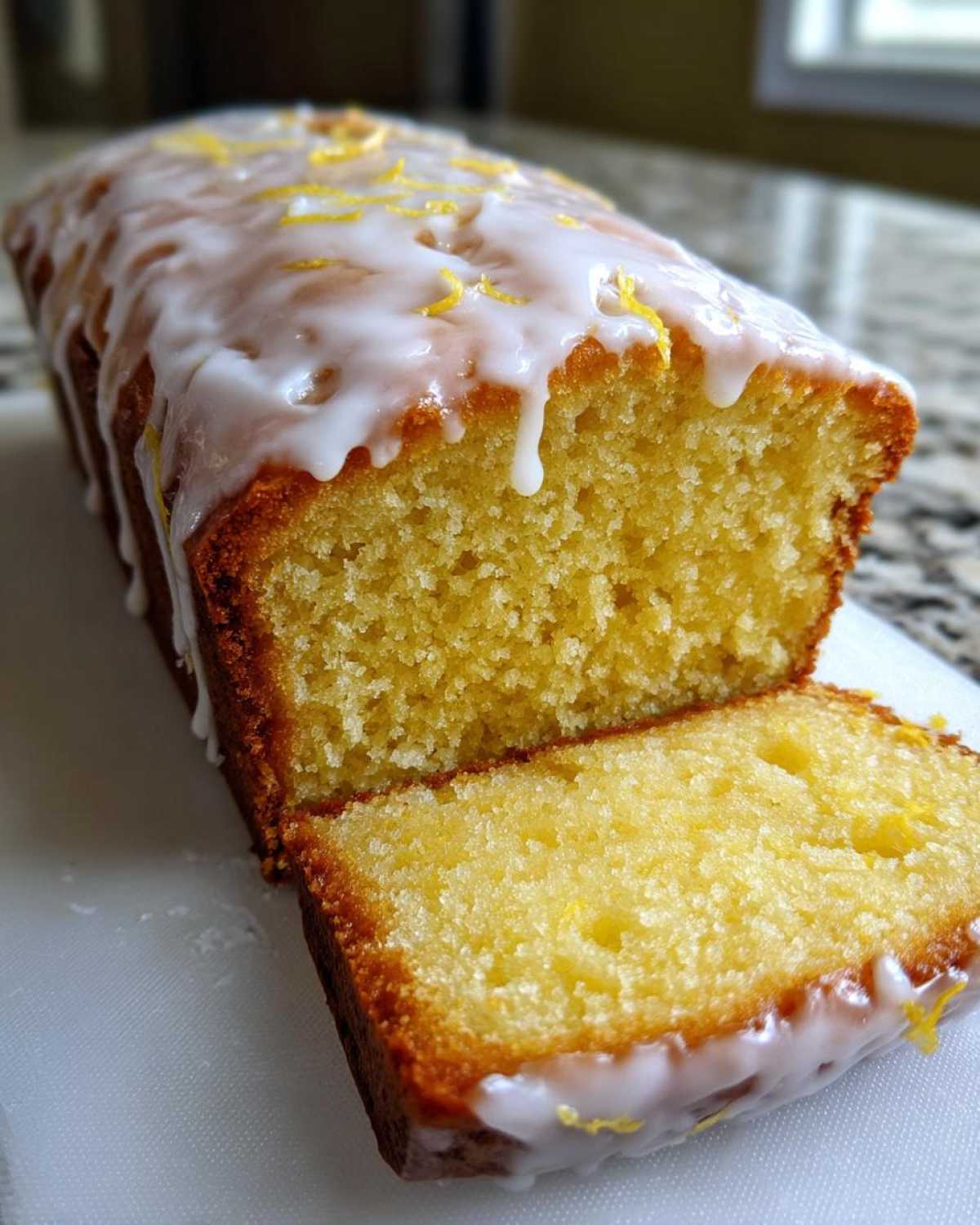 A moist slice cut from the Copycat Starbucks Iced Lemon Loaf, topped with thick white glaze and lemon zest.