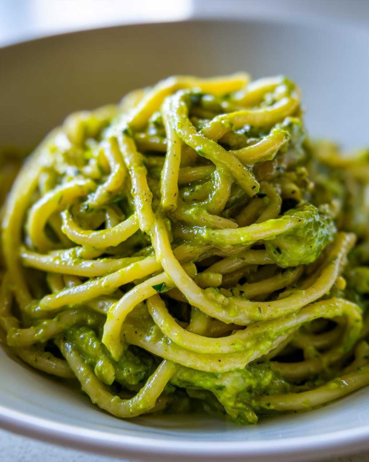 A close-up shot of thick spaghetti coated generously in bright green Creamy Avocado Pasta sauce.