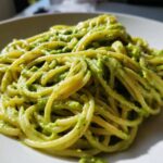 A close-up shot of spaghetti coated in vibrant green Creamy Avocado Pasta sauce served on a white plate.