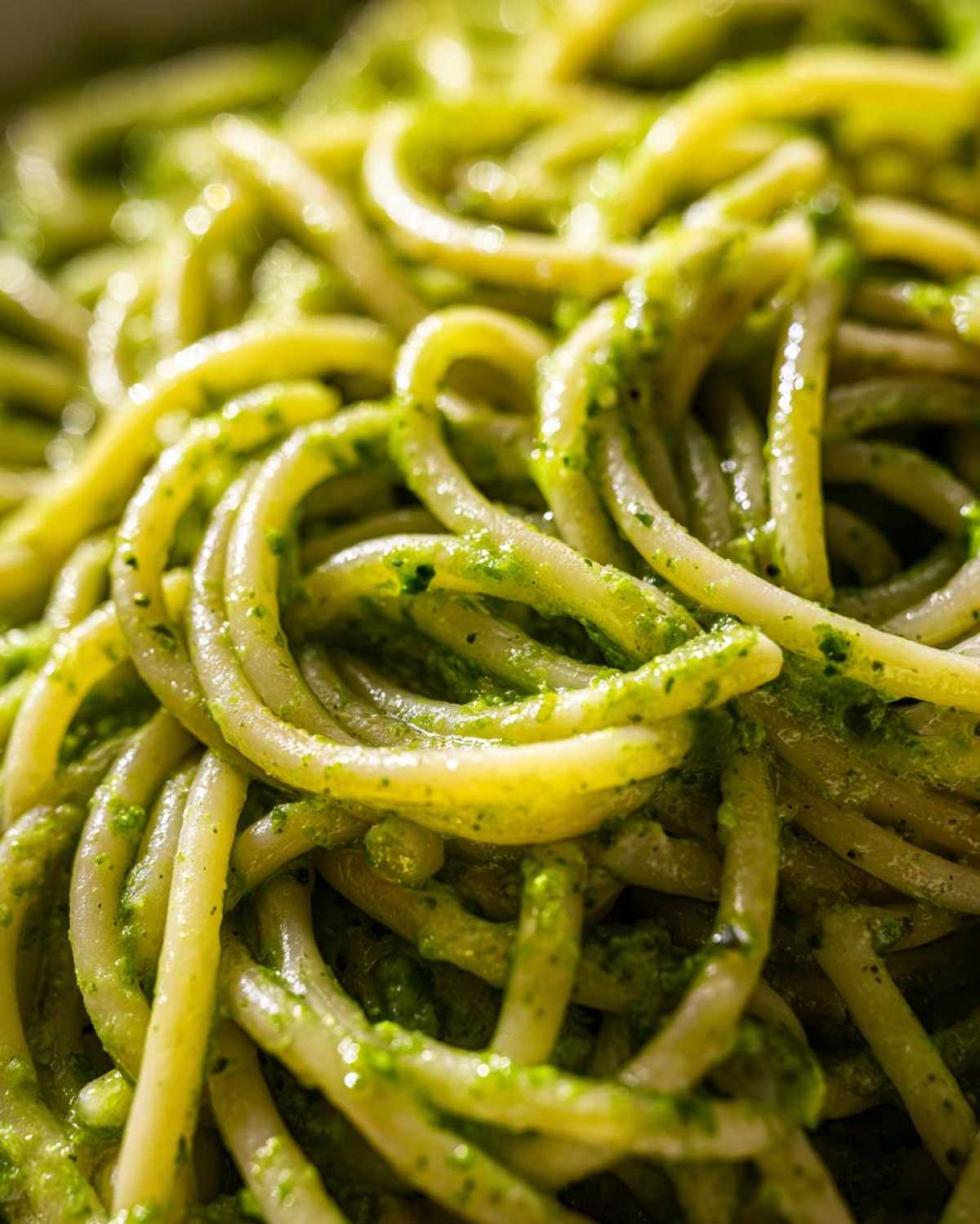 Extreme close-up of thick spaghetti noodles coated in vibrant green Creamy Avocado Pasta sauce.