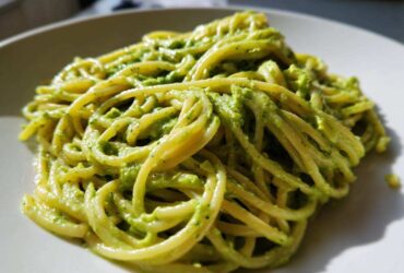 A close-up shot of spaghetti coated in vibrant green Creamy Avocado Pasta sauce served on a white plate.