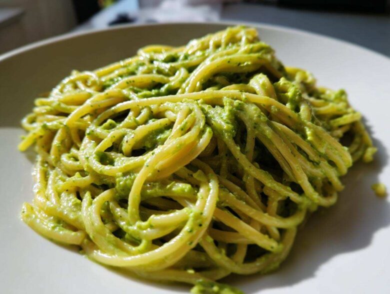 A close-up shot of spaghetti coated in vibrant green Creamy Avocado Pasta sauce served on a white plate.