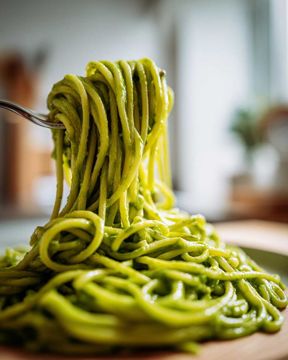A fork lifts a tangle of spaghetti coated heavily in bright green Creamy Avocado Pasta sauce.