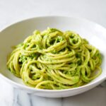 Close-up of spaghetti tossed in vibrant green, creamy avocado pasta sauce, served in a white bowl.