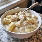 A close-up of a white bowl filled with rich Creamy Chicken Gnocchi Soup, topped with dried herbs.