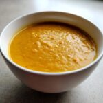 Close-up of a white bowl filled with thick, vibrant orange Creamy Coconut Lentil Soup.