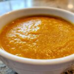 Close-up of a thick, vibrant orange Creamy Coconut Lentil Soup served in a white bowl.