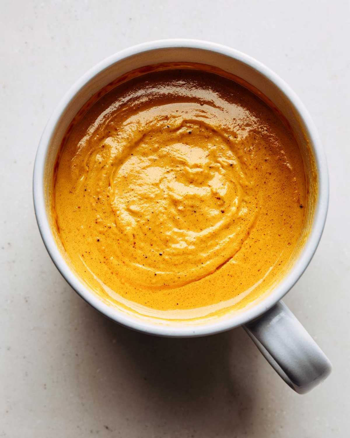 Overhead view of thick, vibrant orange Creamy Coconut Lentil Soup with a swirl pattern in a light gray mug.