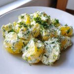 Close-up of chunks of yellow potato coated in a creamy dressing heavily mixed with fresh dill, served on a white plate, showcasing the Creamy Dill Potato Salad.
