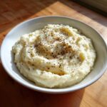A white bowl filled with fluffy Creamy Garlic Mashed Cauliflower, topped generously with cracked black pepper.