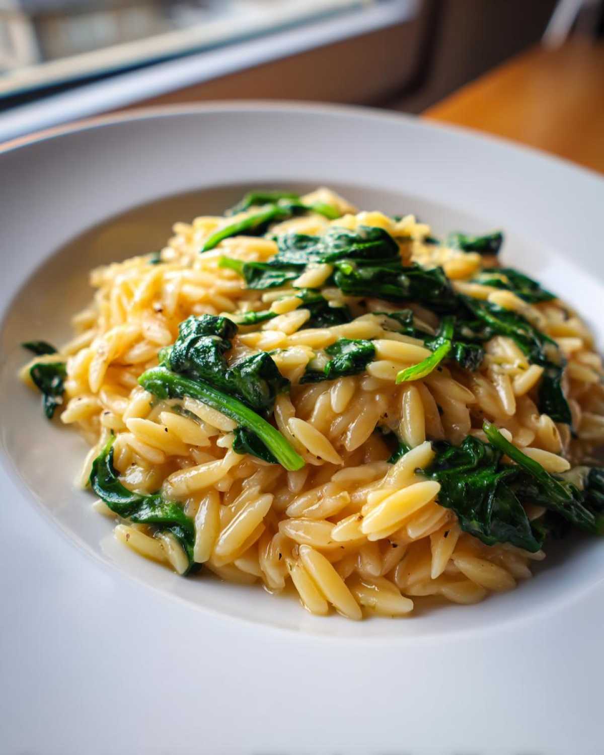Close-up of Creamy Garlic Parmesan Orzo with Spinach served in a white bowl.