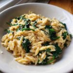 Close-up of a white bowl filled with Creamy Garlic Parmesan Orzo with Spinach, topped with grated cheese.