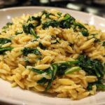 A close-up of a bowl of Creamy Garlic Parmesan Orzo with Spinach, topped with grated cheese.