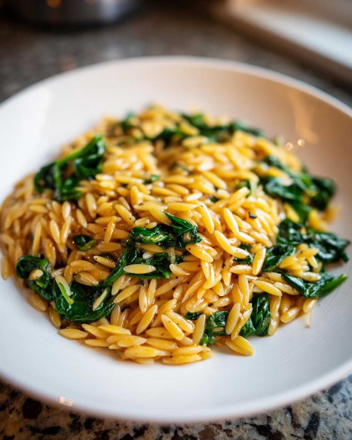 A close-up of creamy garlic parmesan orzo with spinach served in a white bowl.