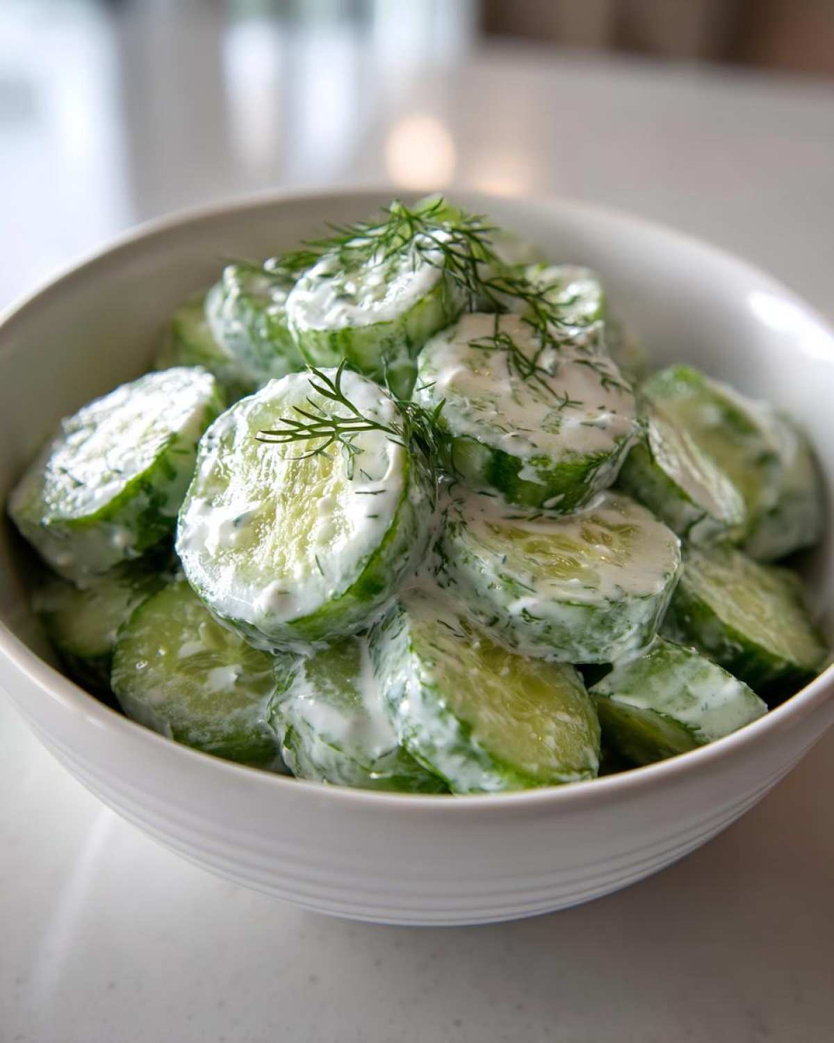 Close-up of sliced cucumbers coated in a creamy dressing, garnished with fresh dill, ready to serve as Creamy German Cucumber Salad.