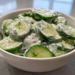 Close-up of sliced cucumbers coated in a creamy white dressing with fresh dill, representing Creamy German Cucumber Salad.