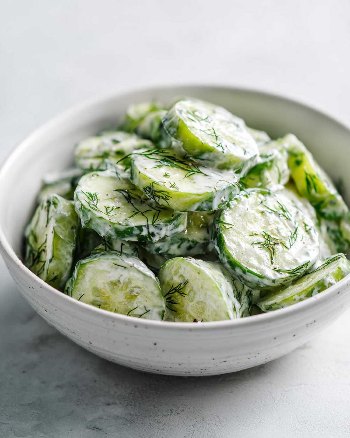 Close-up of sliced cucumbers coated in a white, creamy dressing and fresh dill, showcasing the Creamy German Cucumber Salad.