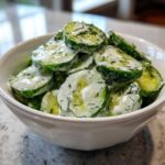 A white bowl filled with slices of Creamy German Cucumber Salad coated in a white dressing and fresh dill.