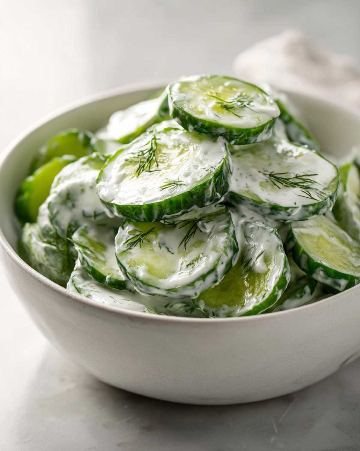 Close-up of sliced cucumbers coated in a white, creamy dressing and garnished with fresh dill, representing Creamy German Cucumber Salad.