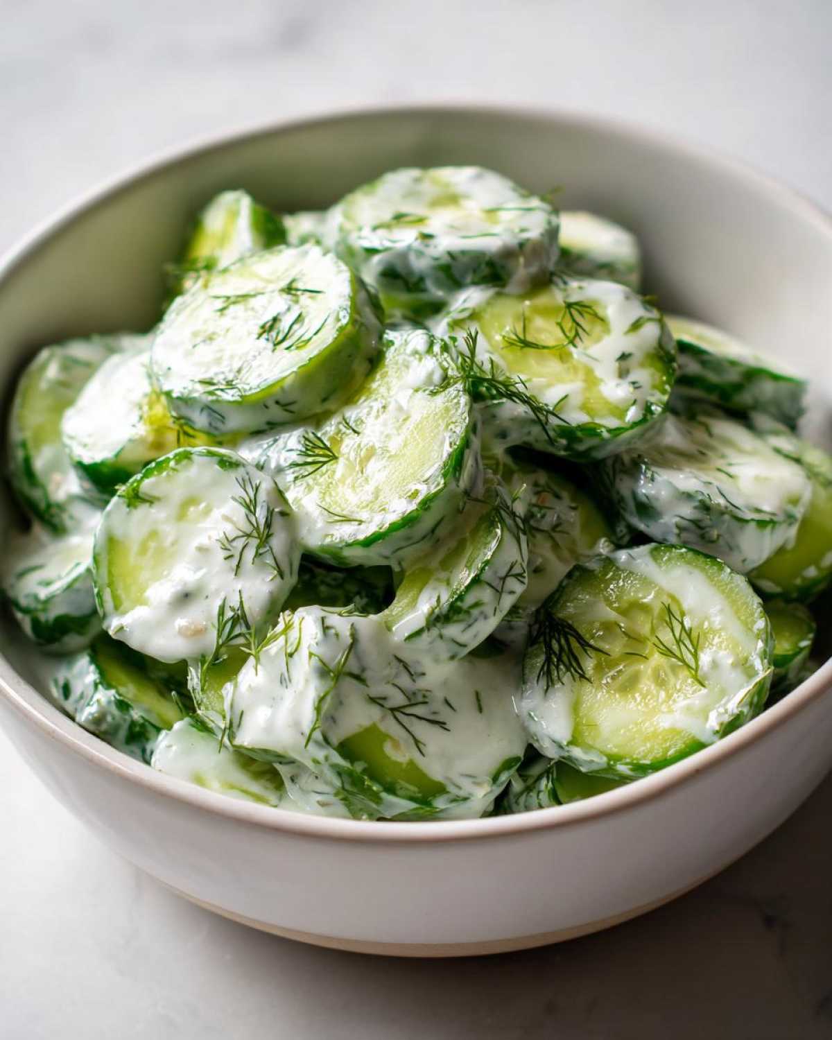 Close-up of sliced cucumbers coated in a creamy dressing and fresh dill, ready to serve, showcasing the Creamy German Cucumber Salad.