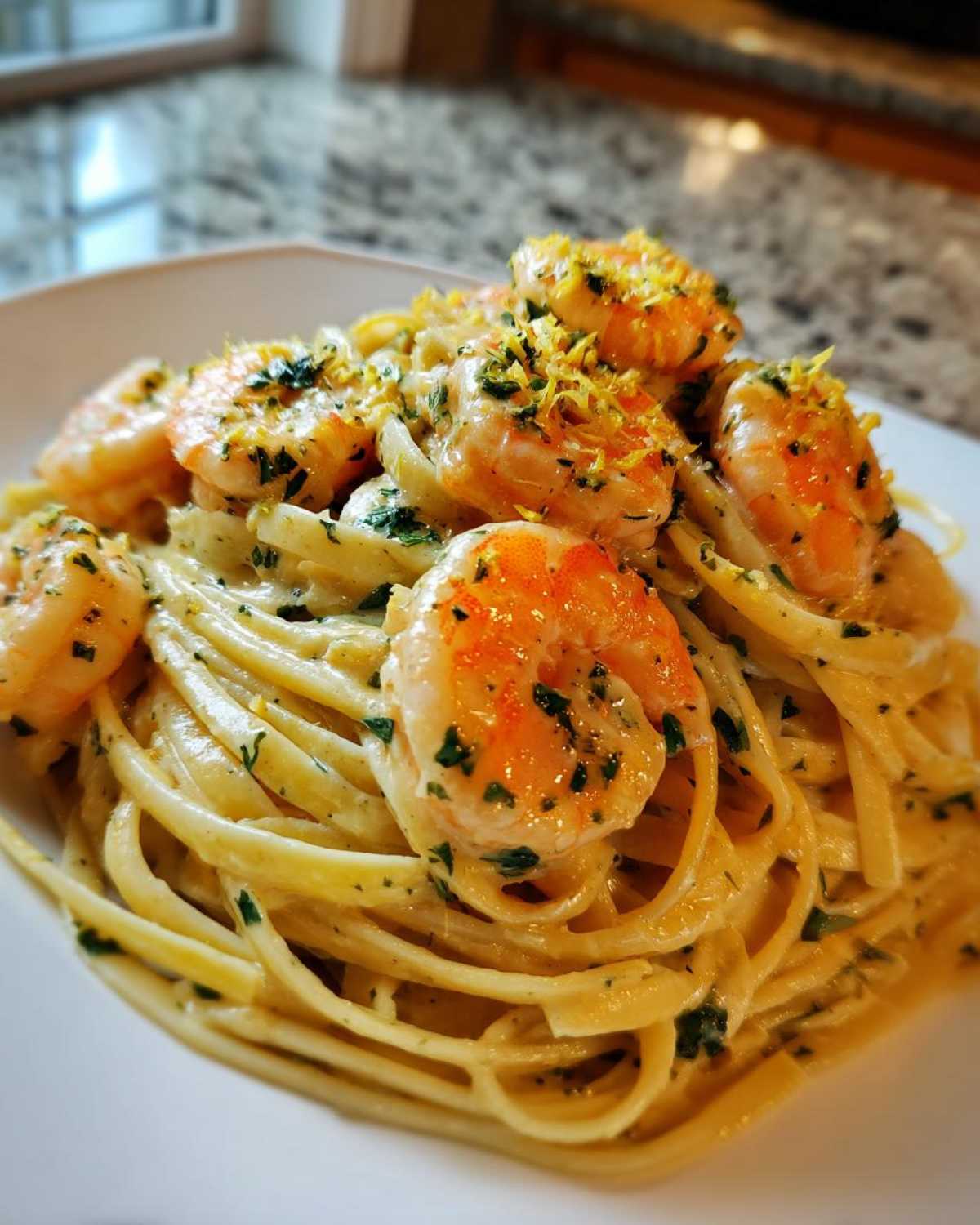 A close-up of creamy lemon garlic shrimp pasta, topped with bright orange shrimp and lemon zest.