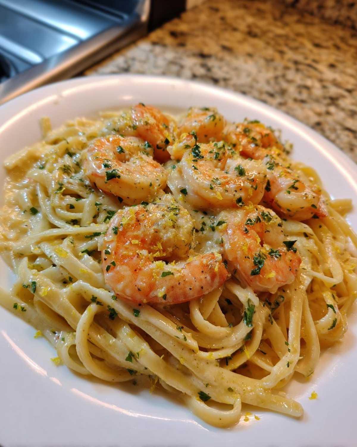 Close-up of a white plate filled with Creamy Lemon Garlic Shrimp Pasta, topped with large shrimp and lemon zest.