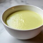 Close-up of a white bowl filled with smooth, pale green Creamy Potato Leek Soup.