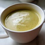 Close-up of a white mug filled with smooth, pale green Creamy Potato Leek Soup, lightly seasoned.