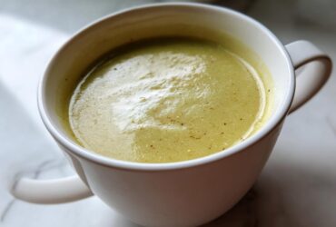 Close-up of a white mug filled with smooth, pale green Creamy Potato Leek Soup, lightly seasoned.