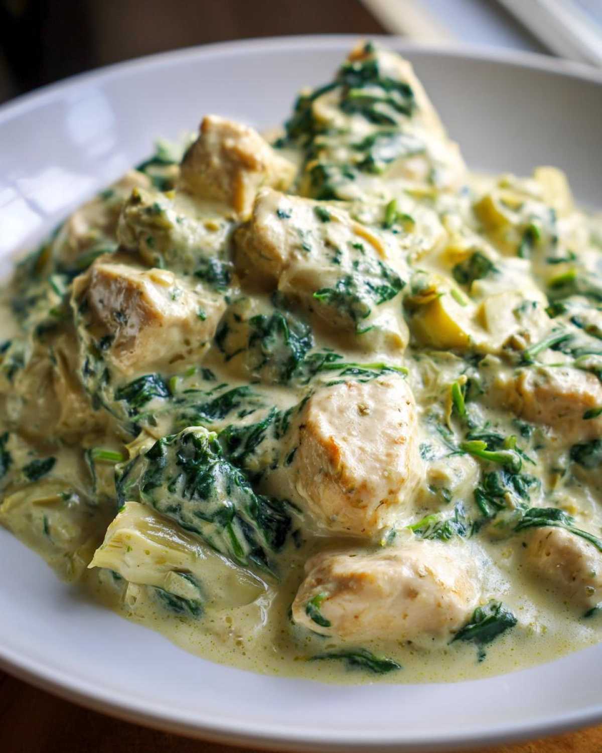Close-up of chunks of chicken breast smothered in a rich, creamy sauce with spinach and artichoke hearts, part of the Creamy Spinach Artichoke Chicken Skillet.