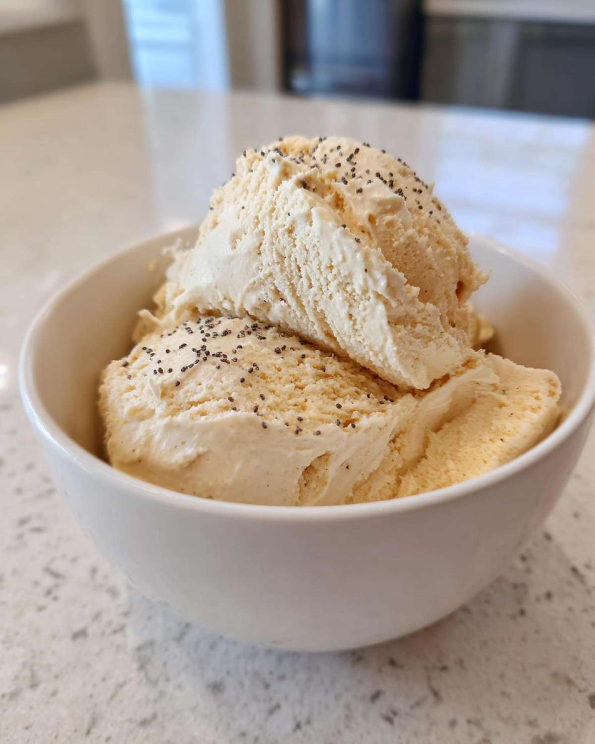 Two scoops of creamy vanilla protein smoothie bowl topped with tiny black seeds in a white bowl.