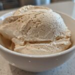 Close-up of thick, creamy vanilla protein smoothie bowl mixture scooped into a white bowl, showing vanilla bean specks.