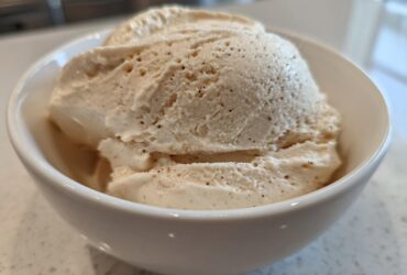 Close-up of thick, creamy vanilla protein smoothie bowl mixture scooped into a white bowl, showing vanilla bean specks.