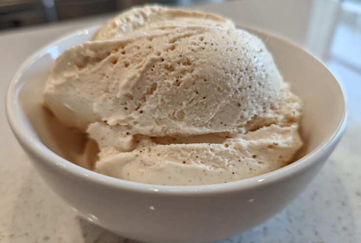Close-up of thick, creamy vanilla protein smoothie bowl mixture scooped into a white bowl, showing vanilla bean specks.