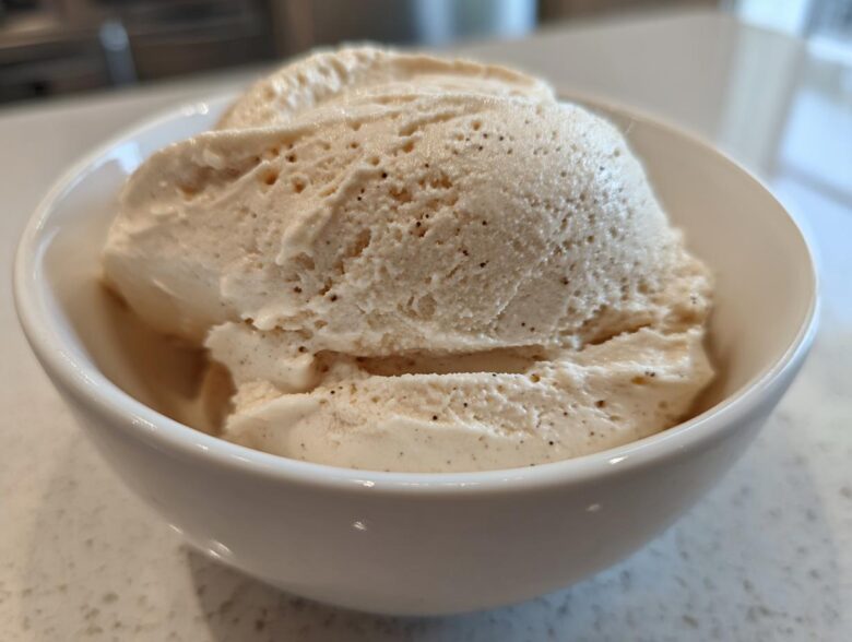 Close-up of thick, creamy vanilla protein smoothie bowl mixture scooped into a white bowl, showing vanilla bean specks.