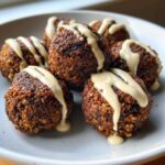 Close-up of several golden brown, crispy air fryer falafel balls drizzled generously with creamy tahini sauce.