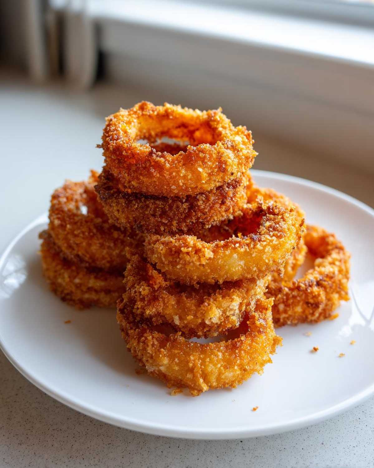 A stack of golden brown, crispy Air Fryer Onion Rings piled high on a white plate.