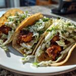 Three Crispy Baked Fish Tacos loaded with seasoned fish and bright lime slaw on a white plate.