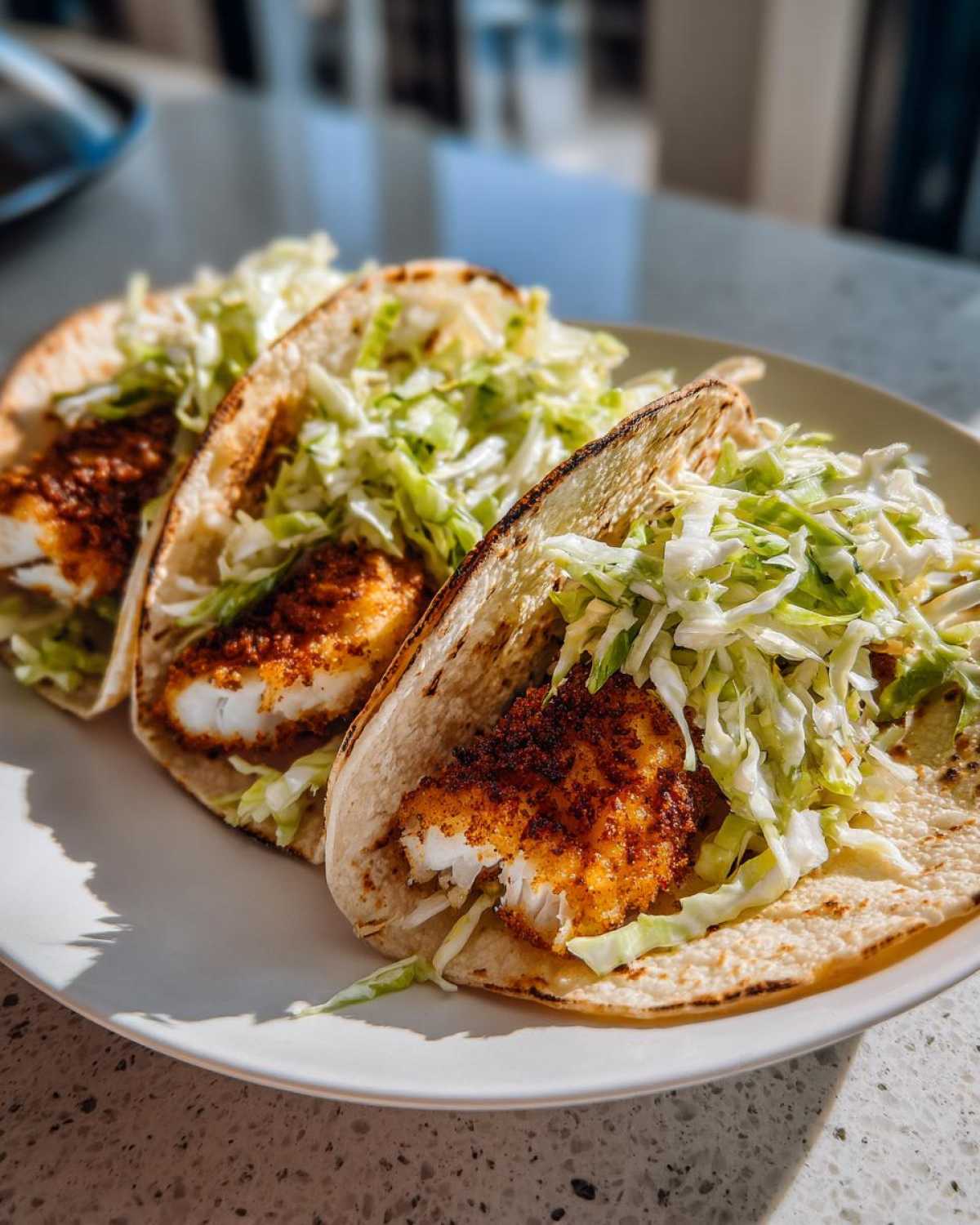 Three Crispy Baked Fish Tacos filled with flaky fish and topped with shredded lime slaw on a white plate.
